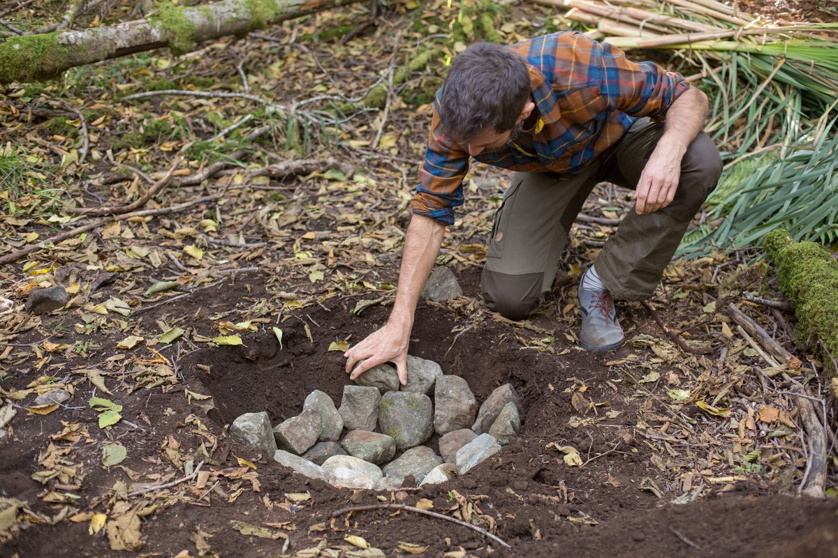 Sascha Borrée legt Steine in einem Wald zusammen in ein Loch, um eine Feuerstelle zu bilden. 