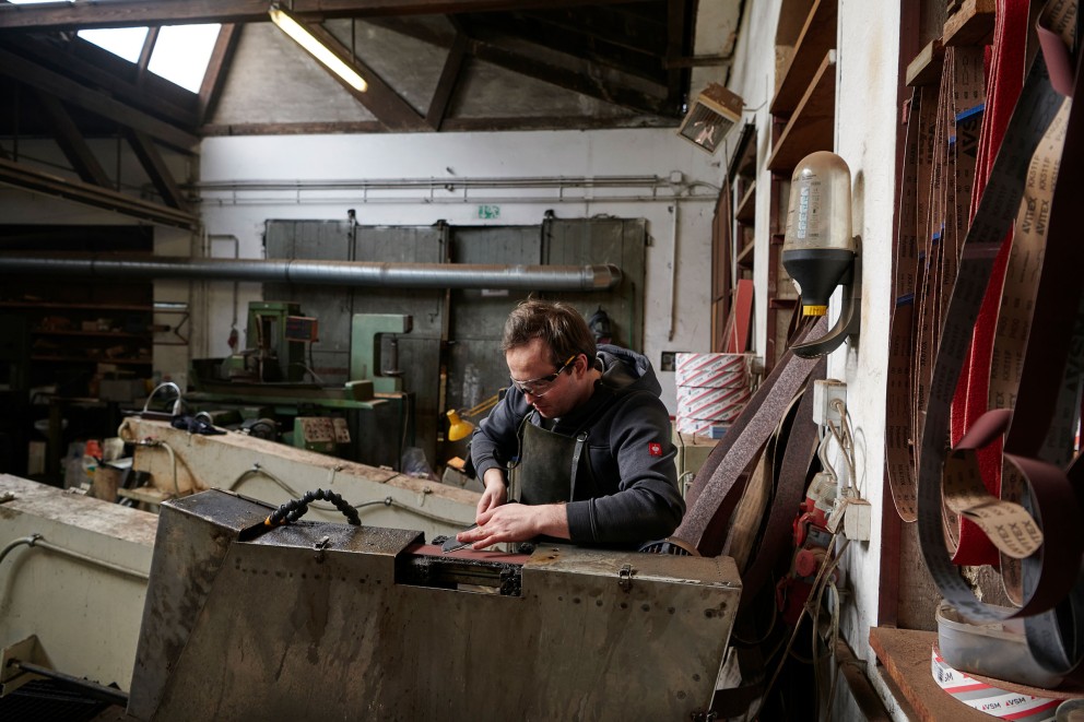 
			Florian schleift ein Messer an einer von ihm selbst entworfenen Schleifmaschine in seiner Werkstatt.

		