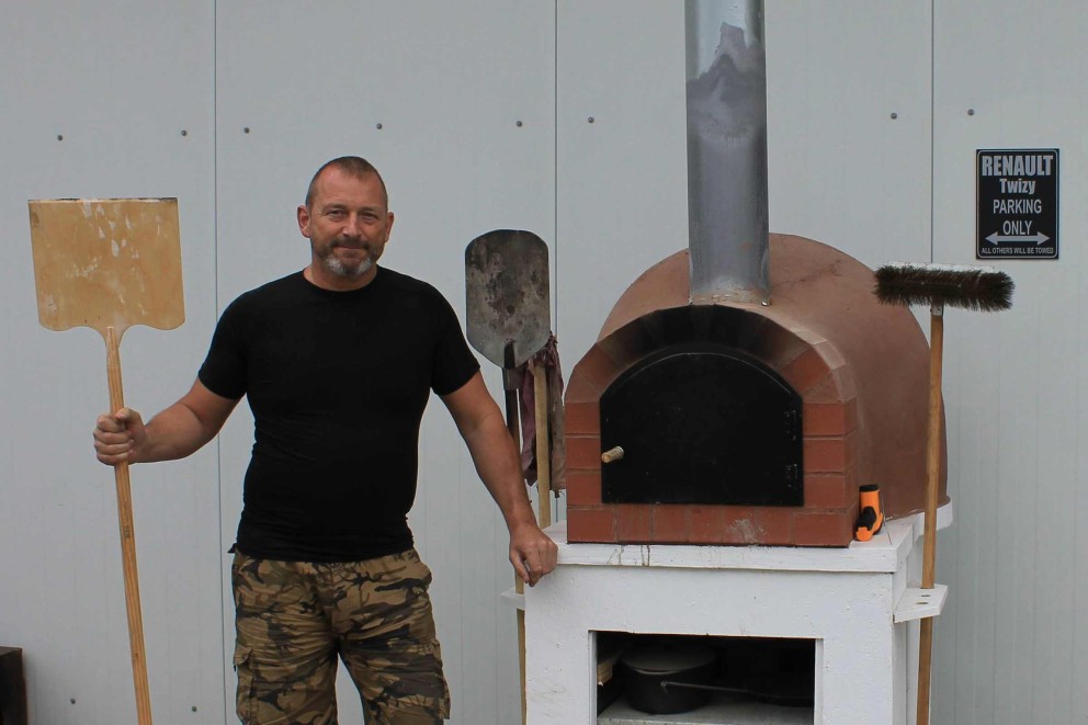 
			Christian Staffler steht neben seinem selbstgebauten Pizzaofen aus selbstgemachten Tonziegeln und Europaletten.

		