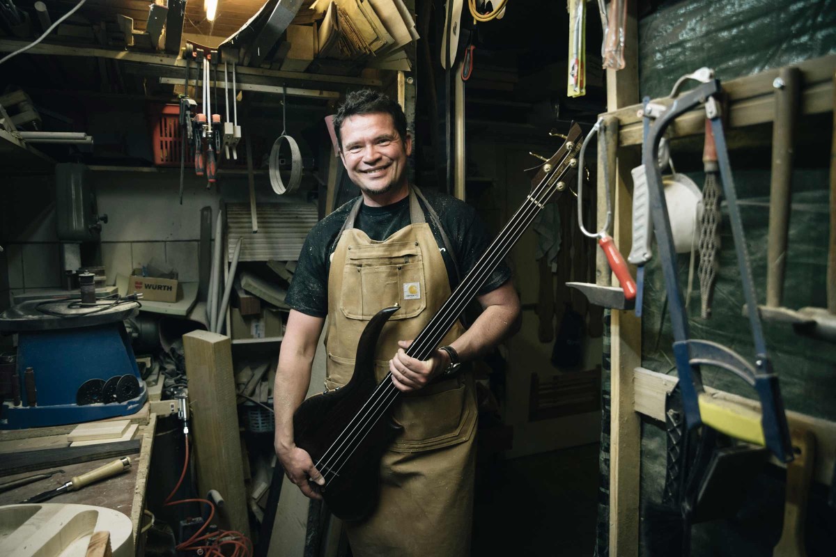 Mike Bolz aus Wolfsburg steht in seiner Werkstatt und hält seinen selbst gebauten E Bass, „Hornbass“ genannt, in den Händen. 
