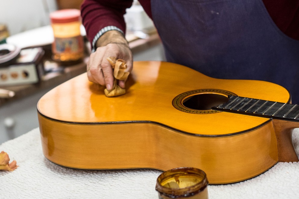 
				Der Gitarrenbauer José Rodríguez Peña verteilt Schellack mit einem Polierballen in kreisenden Bewegungen auf dem Gitarrenkörper

			