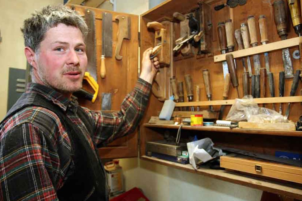 
			Martin vor einem Schrank mit Feilen, Hobeln und Sägen in seiner Werkstatt.

		