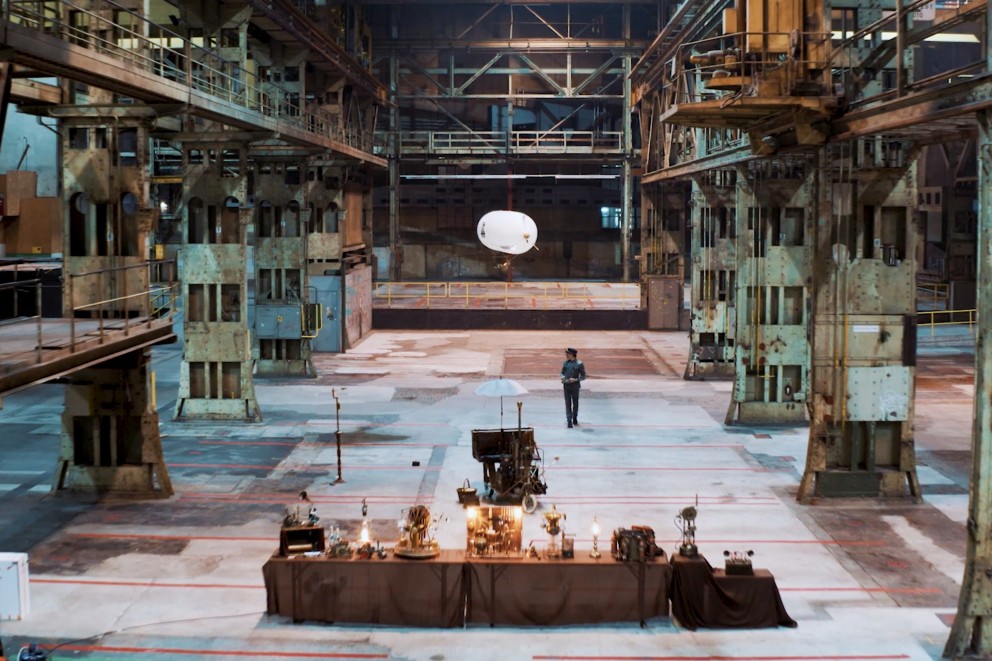 
			Raphaelius fliegt mit einem Helium Luftschiff durch eine große Industriehalle

		