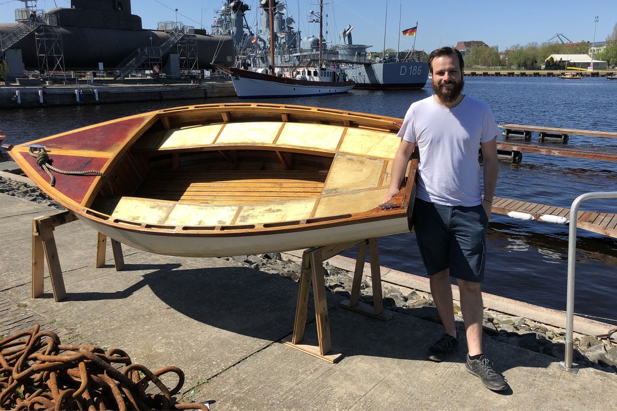 Tristan Konrad steht neben seinem selbstgebauten Boot aus Holz 